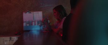 Movie still from “Angel of Anywhere” (2018), directed by James Kicklighter – A woman sitting at a table with a glass in front of her; Medium shot, Over the shoulder angle