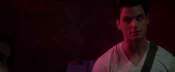 Movie still from “Angel of Anywhere” (2018), directed by James Kicklighter – A man in a white t - shirt is standing in a dark room; Close Up shot, Over the shoulder angle