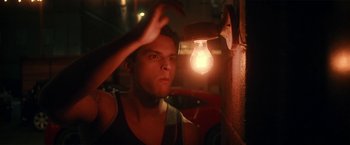 Movie still from “Angel of Anywhere” (2018), directed by James Kicklighter – A man standing in front of a wall with a light hanging from it; Close Up shot, Low angle