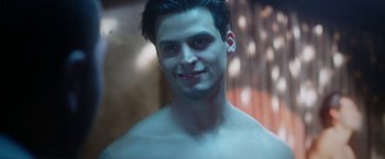 Movie still from “Angel of Anywhere” (2018), directed by James Kicklighter – A young man with no shirt is smiling for the camera; Close Up shot, Low angle