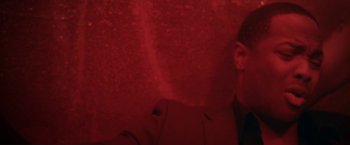 Movie still from “Angel of Anywhere” (2018), directed by James Kicklighter – A man wearing a suit and tie in front of a red wall; Close Up shot, Low angle