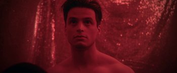Movie still from “Angel of Anywhere” (2018), directed by James Kicklighter – A man with no shirt in front of a red background; Close Up shot, Low angle