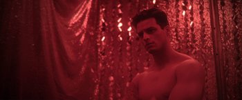 Movie still from “Angel of Anywhere” (2018), directed by James Kicklighter – A man with a tattoo is standing in front of a red curtain; Close Up shot, Low angle