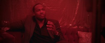 Movie still from “Angel of Anywhere” (2018), directed by James Kicklighter – A man sitting on top of a couch in front of a red wall; Close Up shot, Low angle