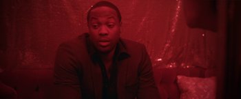 Movie still from “Angel of Anywhere” (2018), directed by James Kicklighter – A man sitting in front of a red background; Close Up shot, Over the shoulder angle
