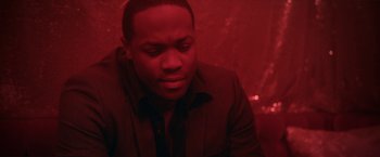Movie still from “Angel of Anywhere” (2018), directed by James Kicklighter – A man sitting in front of a red background; Close Up shot, High angle