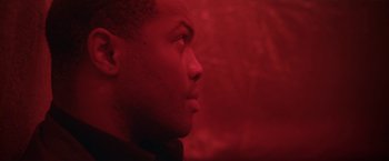 Movie still from “Angel of Anywhere” (2018), directed by James Kicklighter – A person's face in a red room; Close Up shot, Low angle