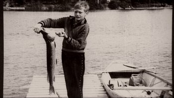 Movie still from “Angst” (1983), directed by Gerald Kargl – A young man holding a fish on a dock; Wide shot, Low angle