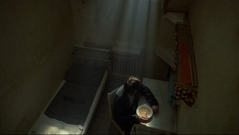 Movie still from “Angst” (1983), directed by Gerald Kargl – A man sitting at a table with a plate in his hand; Wide shot, Overhead angle