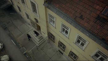 Movie still from “Angst” (1983), directed by Gerald Kargl – An aerial view looking down at a building with a person walking down the stairs; Extreme Wide shot, Overhead angle