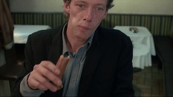 Movie still from “Angst” (1983), directed by Gerald Kargl – A man eating a hot dog while wearing a suit; Close Up shot, High angle