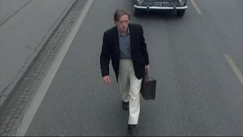 Movie still from “Angst” (1983), directed by Gerald Kargl – A man walking down the street holding a briefcase; Wide shot, Low angle