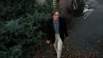 Movie still from “Angst” (1983), directed by Gerald Kargl – A man in a black jacket walking down a street; Medium shot, Low angle