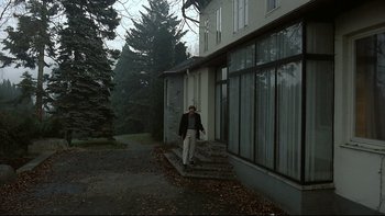 Movie still from “Angst” (1983), directed by Gerald Kargl – A man standing outside of a building on a porch; Wide shot, Low angle