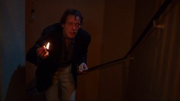 Movie still from “Angst” (1983), directed by Gerald Kargl – A man holding a lit candle in a dark room; Medium shot, Low angle