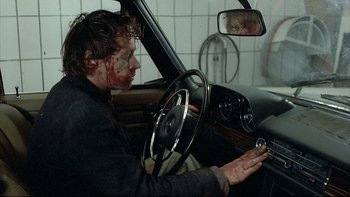 Movie still from “Angst” (1983), directed by Gerald Kargl – A man with blood on his face driving in a car; Medium shot, Over the shoulder angle