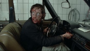 Movie still from “Angst” (1983), directed by Gerald Kargl – A man in a car with blood on his face; Medium shot, Over the shoulder angle