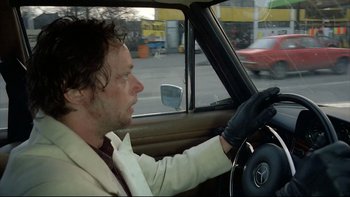 Movie still from “Angst” (1983), directed by Gerald Kargl – A man driving a car in the street wearing gloves; Close Up shot, Low angle