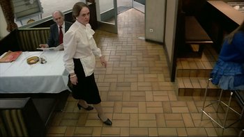 Movie still from “Angst” (1983), directed by Gerald Kargl – A woman standing in front of a table with a man sitting in the background; Medium shot, High angle