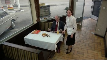 Movie still from “Angst” (1983), directed by Gerald Kargl – A man sitting at a table next to a woman in a restaurant; Wide shot, High angle