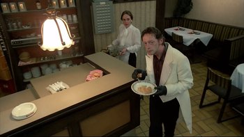 Movie still from “Angst” (1983), directed by Gerald Kargl – A man holding a plate of food in a restaurant; Medium shot, Low angle