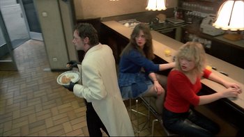 Movie still from “Angst” (1983), directed by Gerald Kargl – A man and two women sitting at a counter; Medium shot, Over the shoulder angle