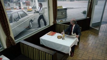 Movie still from “Angst” (1983), directed by Gerald Kargl – A man sitting at a table in front of a window; Wide shot, High angle