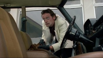 Movie still from “Angst” (1983), directed by Gerald Kargl – A man in a suit and tie fixing a car seat; Medium shot, Low angle