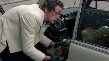 Movie still from “Angst” (1983), directed by Gerald Kargl – A man holding the door of a car with a dog in it; Close Up shot, High angle