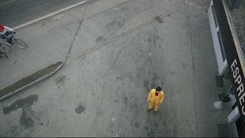 Movie still from “Angst” (1983), directed by Gerald Kargl – A man in a yellow rain suit standing in the street; Extreme Wide shot, Overhead angle