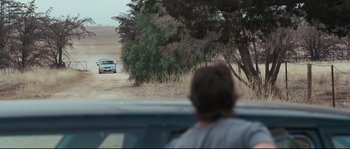 Movie still from “Animal Kingdom” (2010), directed by David Michôd – A man driving a car down a dirt road near a tree; Extreme Wide shot, Over the shoulder angle