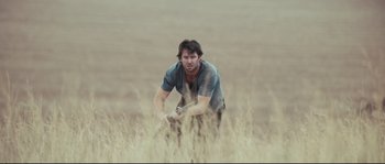 Movie still from “Animal Kingdom” (2010), directed by David Michôd – A man kneeling down in a field holding a knife; Wide shot, Low angle