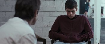 Movie still from “Animal Kingdom” (2010), directed by David Michôd – A man sitting in front of another man in front of a brick wall; Medium shot, Over the shoulder angle