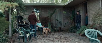 Movie still from “Animal Kingdom” (2010), directed by David Michôd – Two people and a dog sitting in a yard; Wide shot, Over the shoulder angle