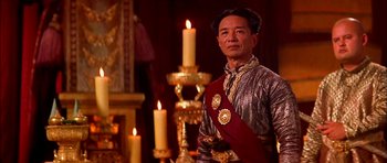 Movie still from “Anna and the King” (1999), directed by Andy Tennant – A man wearing a red sash standing in front of candles; Medium shot, Low angle