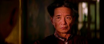 An older asian man wearing a red and black shirt