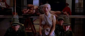 Movie still from “Anna and the King” (1999), directed by Andy Tennant – A woman with a shaved head standing in front of a group of people; Medium shot, Over the shoulder angle