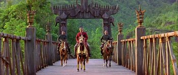 Movie still from “Anna and the King” (1999), directed by Andy Tennant – Three men riding horses across a bridge in front of a forest; Wide shot, Low angle