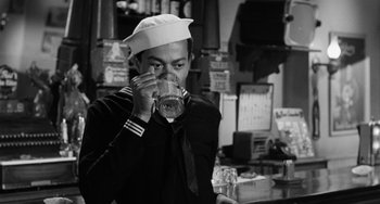 Movie still from “Anna Lucasta” (1958), directed by Arnold Laven – A man in a sailor's uniform drinking a glass of water; Medium shot, Over the shoulder angle