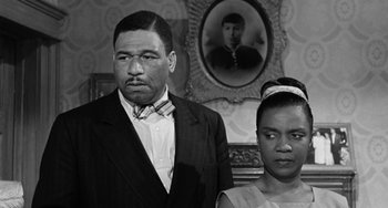 Movie still from “Anna Lucasta” (1958), directed by Arnold Laven – A man and a woman standing next to each other in front of a portrait; Close Up shot, Low angle