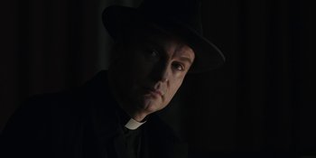 Movie still from “Dark” (2017), created by Baran bo Odar – A man wearing a hat and a priest's outfit; Close Up shot, Low angle
