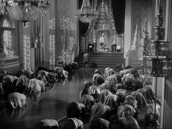 Movie still from “Anna and the King of Siam” (1946), directed by John Cromwell – A group of people kneeling down in front of a chandelier; Extreme Wide shot, High angle