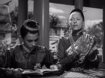 Movie still from “Anna and the King of Siam” (1946), directed by John Cromwell – Two people sitting at a table reading a book; Medium shot, Over the shoulder angle