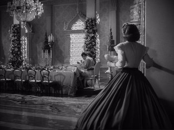 Movie still from “Anna and the King of Siam” (1946), directed by John Cromwell – A black and white photo of a woman in a long dress in front of a dining room table; Wide shot, Over the shoulder angle