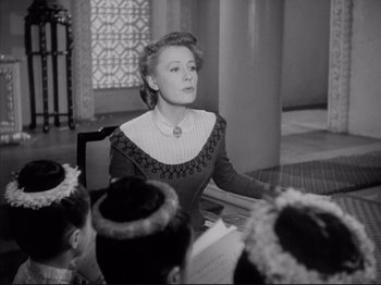 Movie still from “Anna and the King of Siam” (1946), directed by John Cromwell – An old black and white photo of a woman sitting in front of a group of people; Medium shot, Low angle