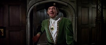Movie still from “Anne of the Thousand Days” (1969), directed by Charles Jarrott – An older man in a green outfit with a gold chain around his neck; Medium shot, Over the shoulder angle