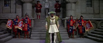 Movie still from “Anne of the Thousand Days” (1969), directed by Charles Jarrott – A man dressed as a king stands in front of a group of people; Wide shot, High angle