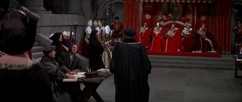 Movie still from “Anne of the Thousand Days” (1969), directed by Charles Jarrott – A man wearing a black robe and a black hat standing in front of a group of people; Wide shot, High angle