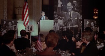 Movie still from “Annie Hall” (1977), directed by Woody Allen – A man is giving a speech in front of an american flag; Medium shot, Over the shoulder angle