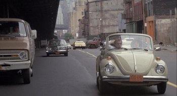 Movie still from “Annie Hall” (1977), directed by Woody Allen – An old car driving down a street past a tall building; Wide shot, Over the shoulder angle